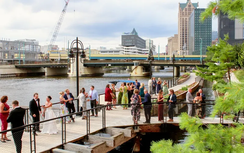 A wedding party and their guests on the Milwaukee Riverwalk with the downtown skyline behind them