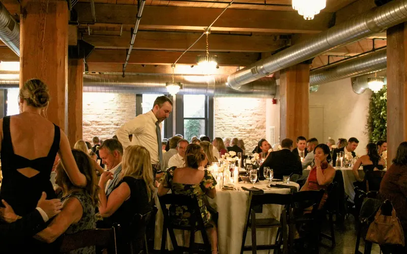 A seated dinner at round tables in a room with timber posts and exposed brick
