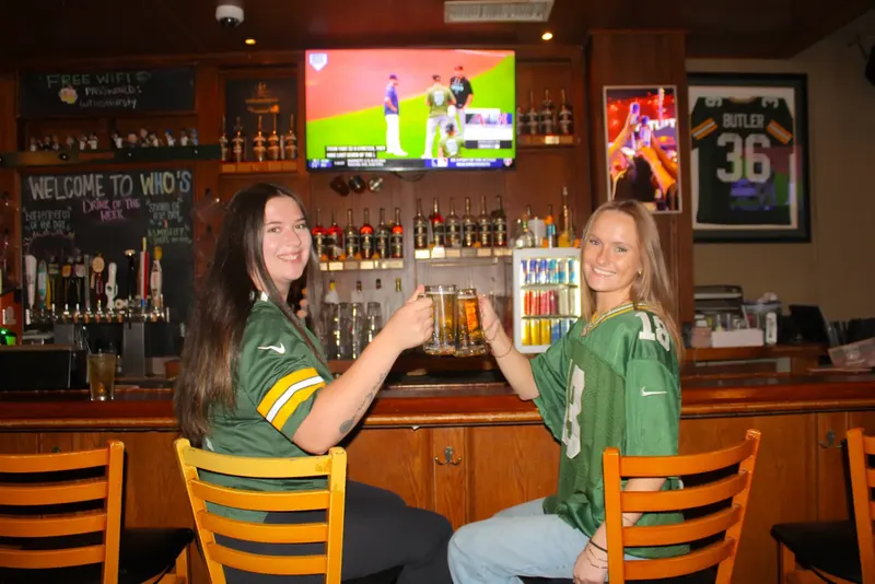 Two fans in Packers jerseys raising beers at the bar inside Who's on Third