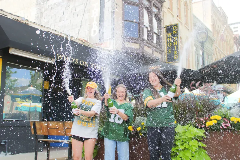 Four friends in Packers gear spraying champagne on the patio outside Who's on Third