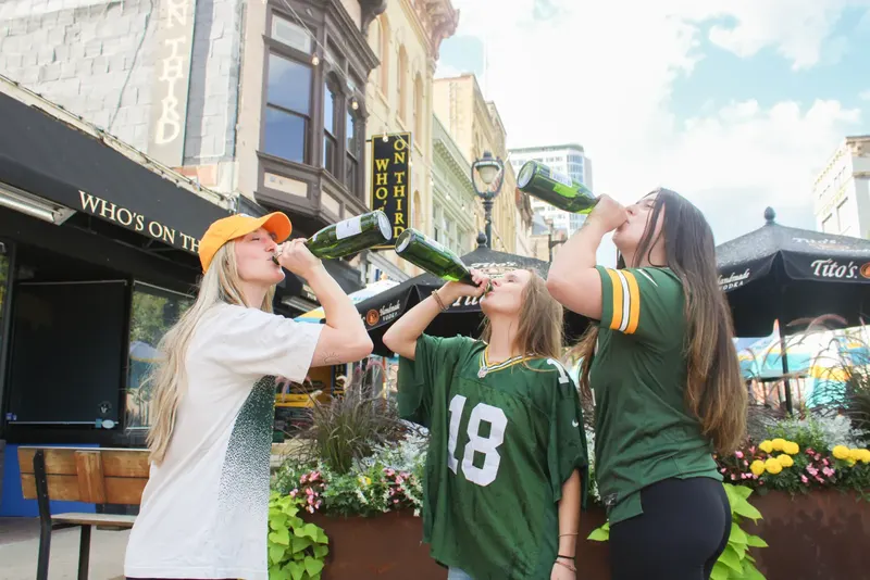 Three friends in Packers jerseys drinking champagne from the bottle outside Who's on Third