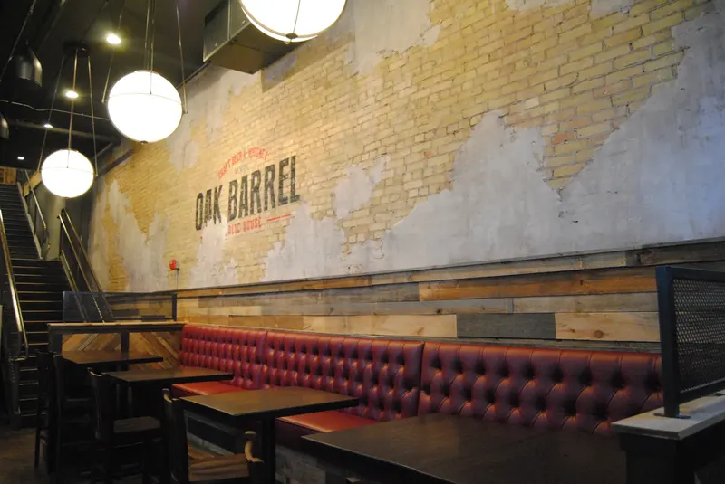 The painted Oak Barrel sign on a cream brick wall above a red tufted banquette and wooden tables